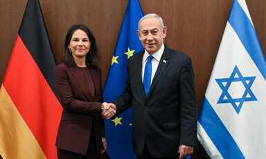 German Foreign Minister Annalena Baerbock clasps hands with Israeli Prime Minister Benjamin Netanyahu in front of German, European Union and Israeli flags 