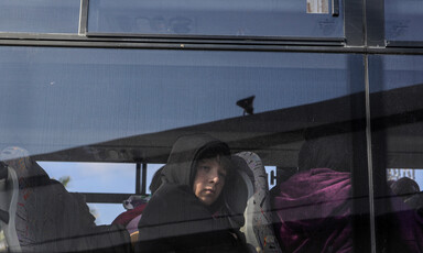 A child is seen looking out the window of a bus. 