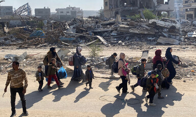 Families with young children carry their belongings past piles of rubble and wreckage