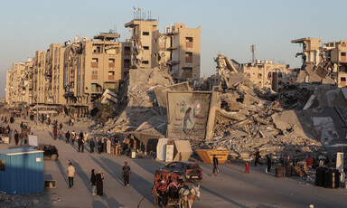 People and donkey carts pass by enormous piles of rubble from bombed buildings