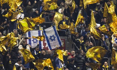 Football fans in a stadium wave yellow and Israeli flags