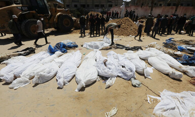 Corpses wrapped in white shrouds are spread across sand ground