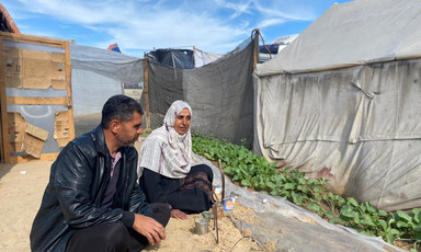 A man and a woman sits next to a strip of cultivated but sandy land