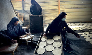 One woman stands and two women sit beside trays of rolled dough in southern Gaza 