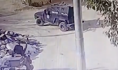 Two teens on a motorcycle parked feet away from armored vehicle 