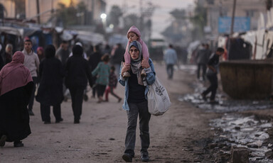 A young woman carries a toddler on her shoulders and holds a bag