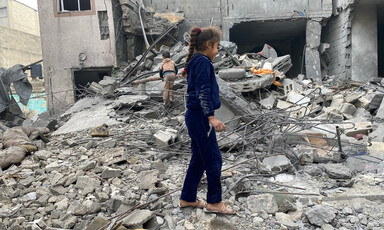 Two young children walk through the rubble of a destroyed house 