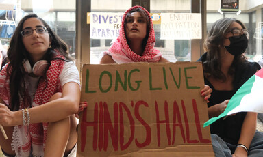 Three young women sit on floor while wearing kaffiyehs and holding sign reading: Long Live Hind's Hall