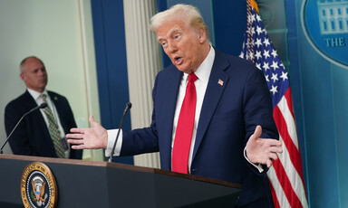 President Donald Trump with hands upraised at podium with man and American flag in background