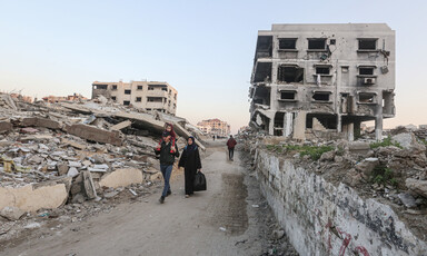 A family walks on a street between destroyed buildings