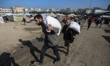 two men carry large bags of flour