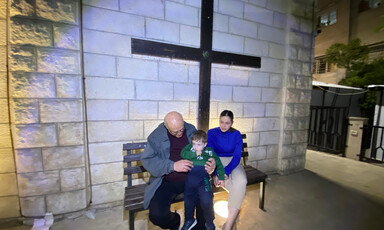 A couple and a toddler sit under a large cross