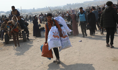 A child with heavy bags amid a crowd of people on foot