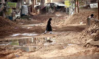 A girl walks amid muddy, damaged roads