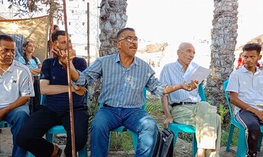 A man speaks and gestures with hands while sitting on a chair on a sunny day