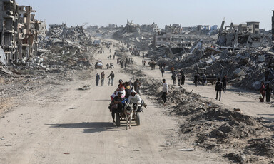 A cart traverses a dust road in a bleak landscape of destroyed buildings