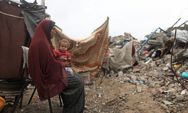 A woman seen in profile sits on a chair with a baby on her lap