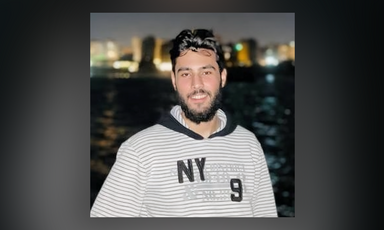 Smiling young man looks at camera with nighttime city skyline in background