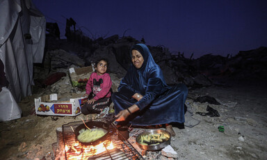 A mother and child prepare food over an open fire