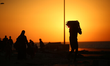 A man in silhouette against a setting sun carries a gas canister