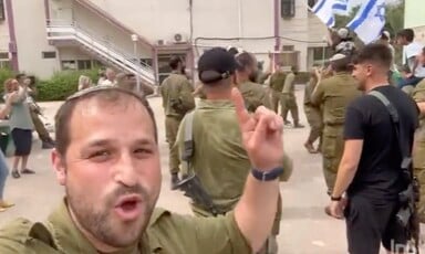 A man in an Israeli army uniform gestures at an Israeli flag