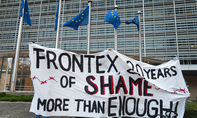 A banner reading Frontex 20 Years of Shame More than Enough beneath the European Union's flags at a protest in Brussels