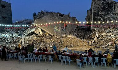People gather under festive lights on a background of destroyed buildings