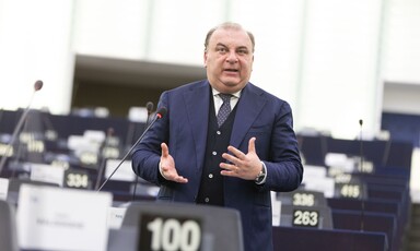 An Italian lawmaker wearing a suit gestures with his hands as he stands and speaks at a podium inside the European Parliament 