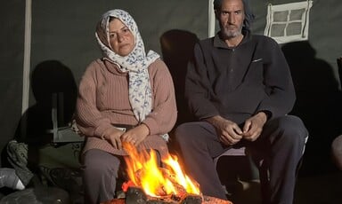 A woman and a man sit behind a fire