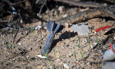 A piece of a weapon with its nose buried in the ground near blades of grass