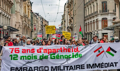 People march in a street holding a large banner and signs