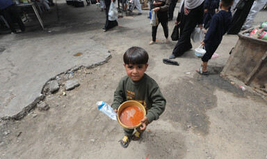 A small child holds up a bowl filled with a reddish liquid.