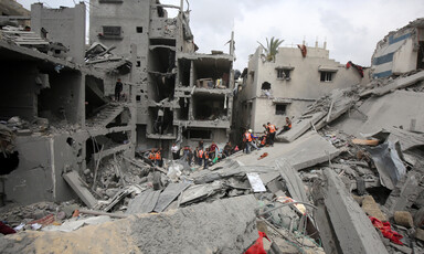 People stand on the top of piles of rubble. Some of them are wearing orange vests.