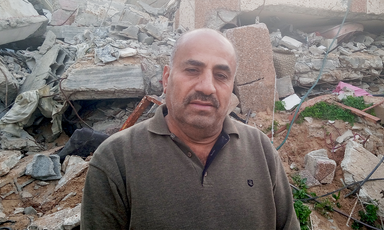 A close-up of man in a collared shirt in front of piles of rubble
