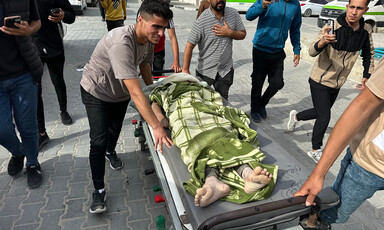 A few men wheel a trolley on which the body of a boy killed by Israel has been laid