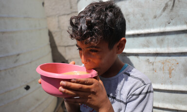 A boy wearing a striped t-shirt lifts a pink bowl to his lips