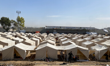 On a sunny day, rows of white tents set up on dirt