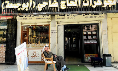 An older man sits in a plastic chair in front of a jewelry shop