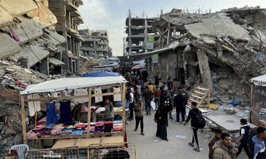 People walk past a small stall amid destroyed buildings