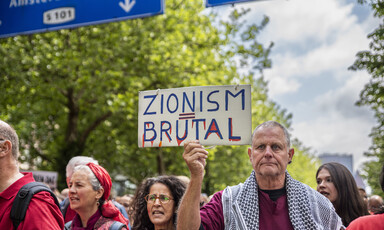 A man holds a placard saying Zionism Equals Brutal surrounded by other protesters