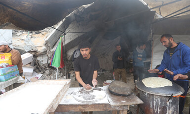 Two people make bread at a stall erected amid a badly damaged refugee camp in Gaza 
