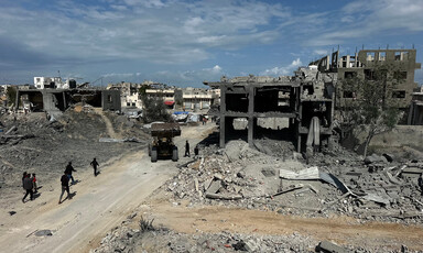 During the daytime, a road runs through bombed-out buildings.