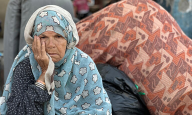 An older woman hold her head in her right hand while sitting in front of personal belongings