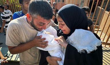 A crying man and woman look at a shrouded baby held by the woman