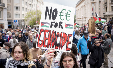 Person holds "No euros for genocide" sign amid large marching crowd