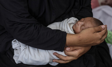 A woman's arms, clothed in black, cradles a sleeping newborn baby wrapped in a white blanket.