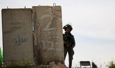 An Israeli soldier wearing helmet stands to the right of a large slab of concrete.