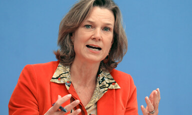 A portrait of a woman wearing a red jacket speaking at an event 