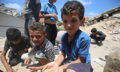 A boy holds out his hands to show the camera pieces of grain he has collected from the ground