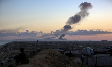 Plumes of dark smoke hover above a sunrise as a man watches.